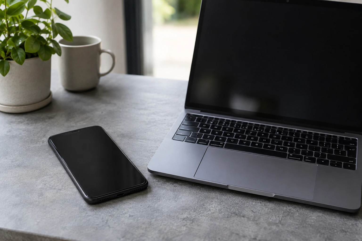 IPhone posé à côté d’un ordinateur portable sur un bureau près d’une fenêtre, tasse et plante visible